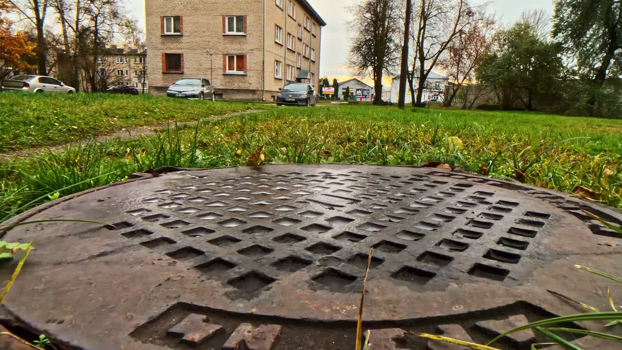 Manhole and grass with urban buildings on cloudy day