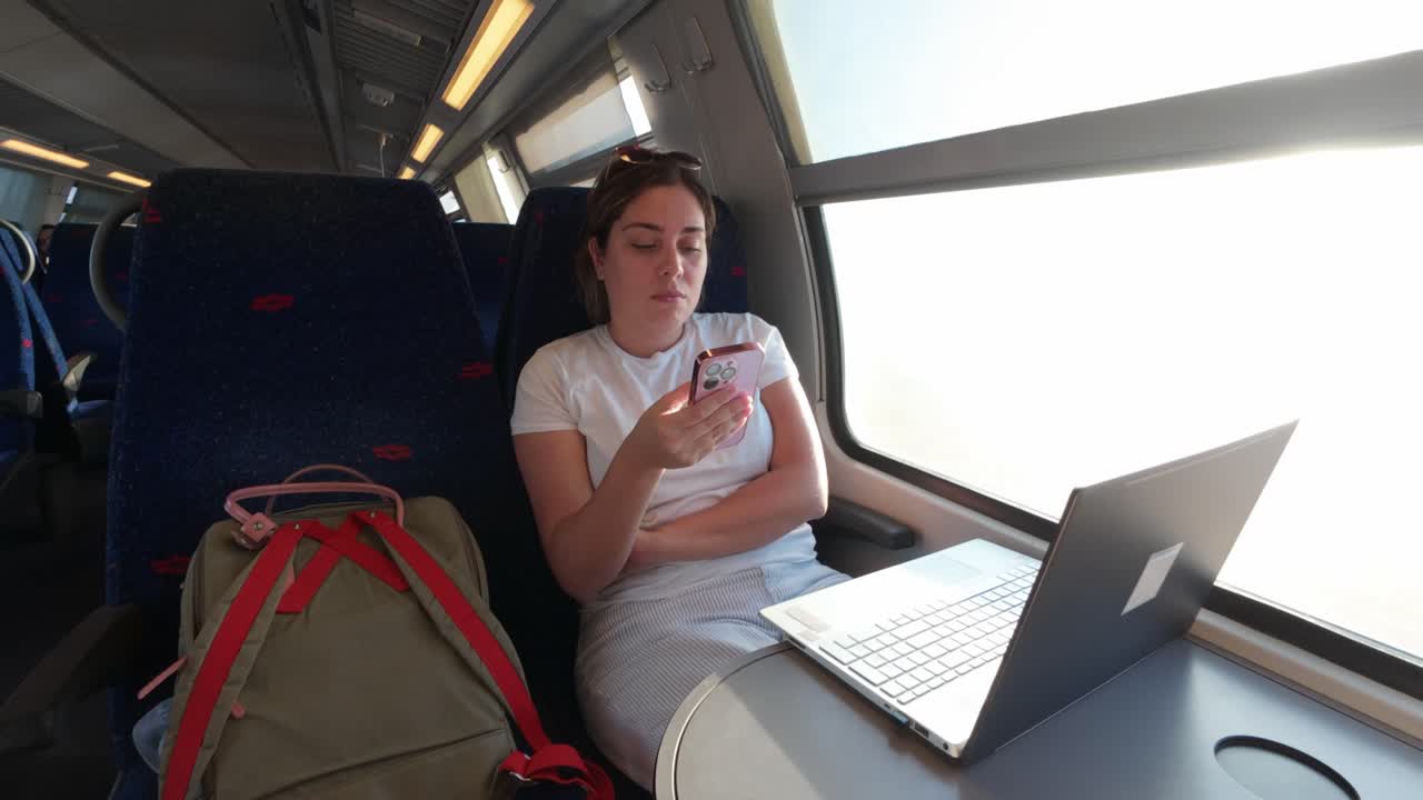 Female Traveler Checking Her Phone on a Train with Laptop