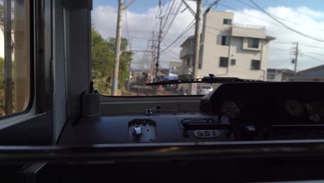 view of buildings and green trees inside the cabin of a train driving on the railway of enoshima dentetsu line in a japanese town in japan - wide shot