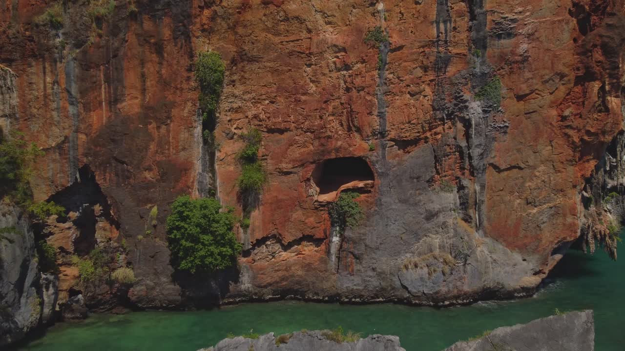 Aerial shot of Ao Nang Beach and its dramatic red limestone cliffs rising above the turquoise sea, with boats and a yacht anchored near the tropical shoreline in Krabi, Thailand.