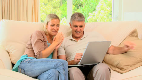 pareja disfrutando de las imágenes en la computadora portátil en el sofá