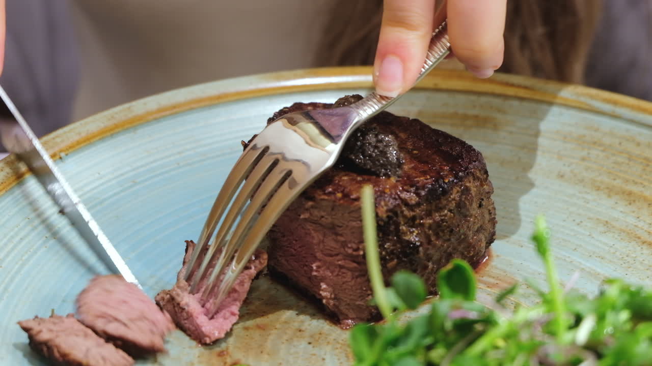 Close up of a woman cutting a piece of filet mignon at a restaurant