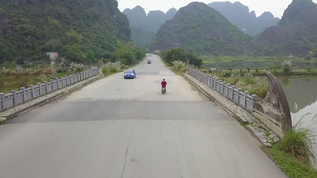 Unique drone follow cam of red shirt motorbiker, oncoming traffic and big limestone mountains