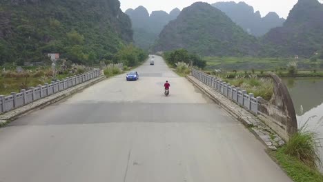 unique drone follow cam of red shirt motorbiker, oncoming traffic and big limestone mountains