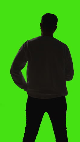 video de vista trasera vertical con silueta de un hombre que responde una llamada en un teléfono móvil de pie contra una pantalla verde con iluminación de bajo nivel