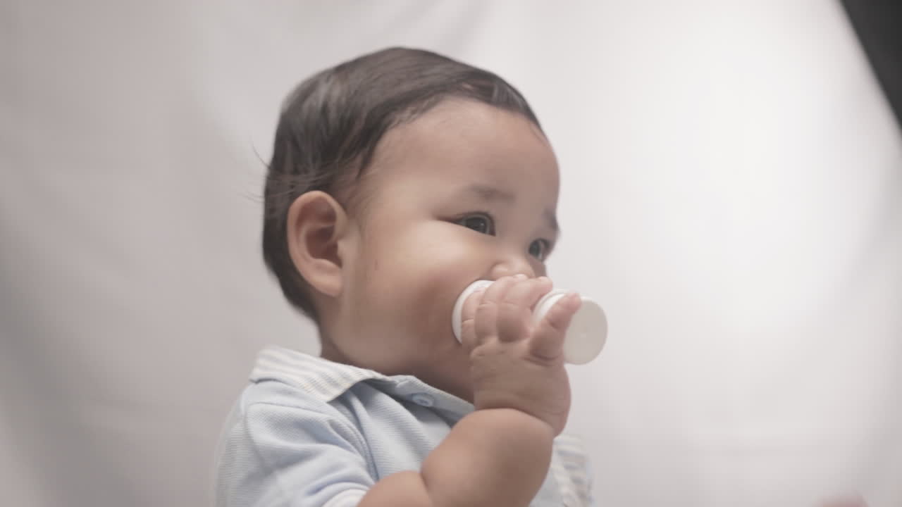 Neonato carino che morde una bottiglia di plastica su sfondo bianco