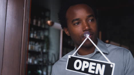 male owner of start up coffee shop or restaurant turning round open sign on door