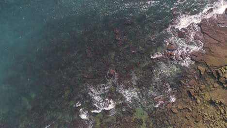 Aerial-top-down-view-of-blue-sea-waves-crashing-over-rocks-in-iconic-Cadiz-bay