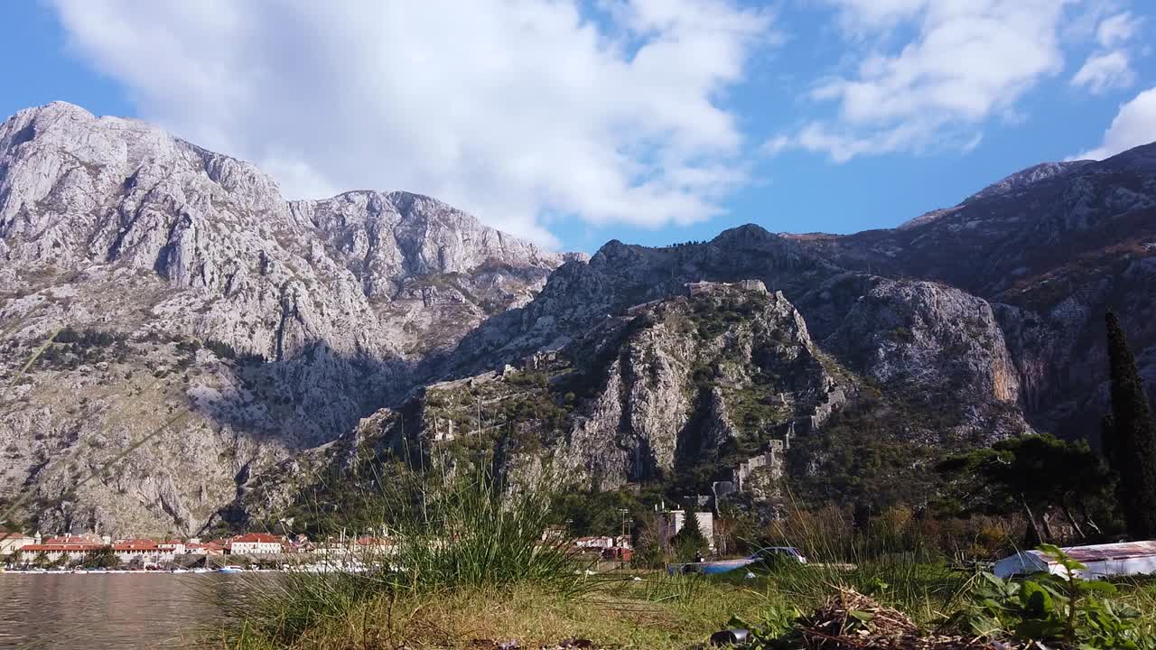 Static shot of mountain range with water in foreground and birds flying. Beautiful white clouds.