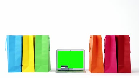 bolsas de compras multicolores y portátil sobre fondo blanco