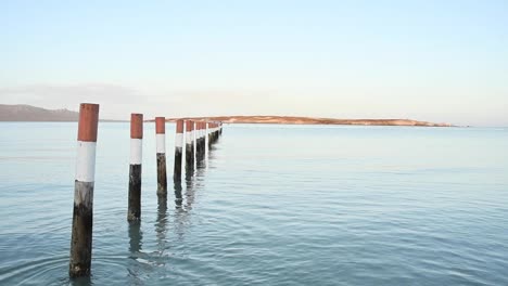 Poles-reflect-against-the-water-of-a-lagoon-with-an-island-in-the-background