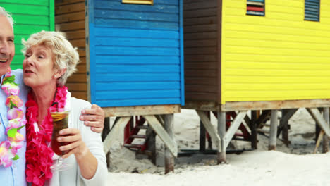 una pareja de mayores tomando una copa cerca de una cabaña de playa colorida