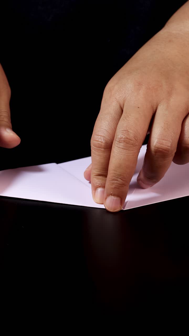 Adult hands carefully fold white paper for origami, close-up, under soft studio lighting