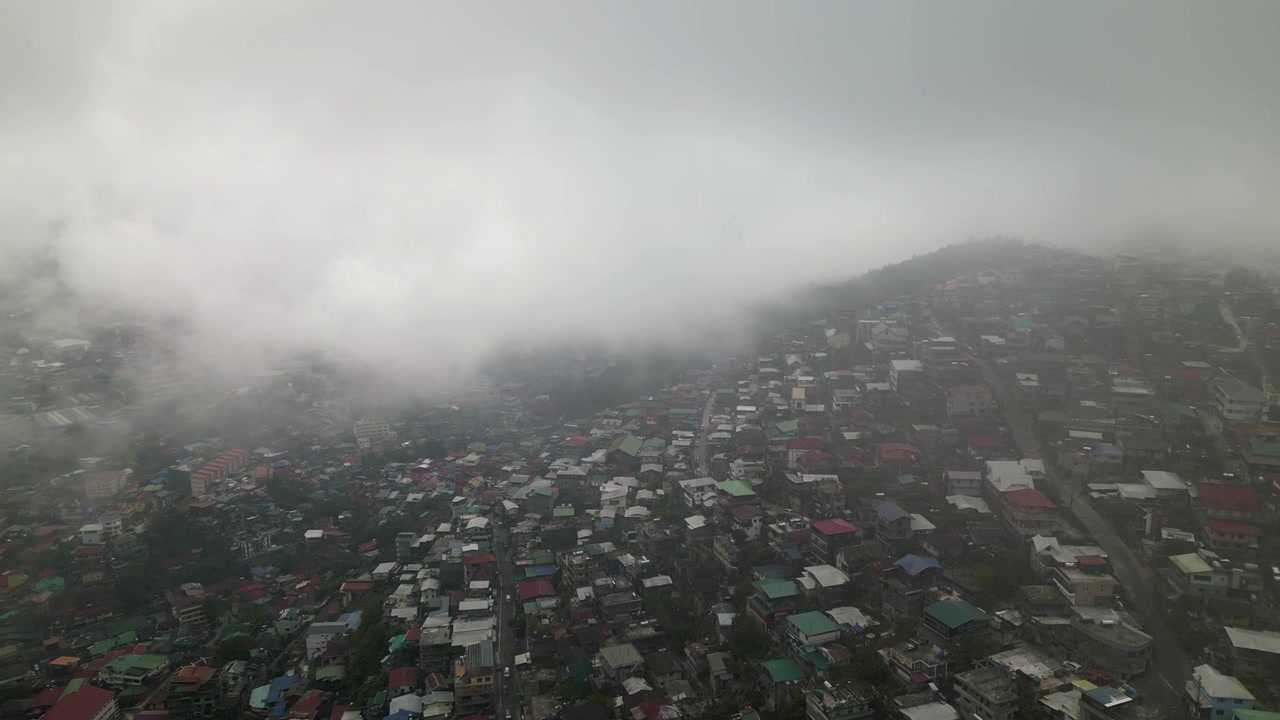 Órbita aérea circulando uma densa comunidade em encosta com telhados coloridos e neblina flutuando sobre a Colina Quirino, Baguio City, Filipinas
