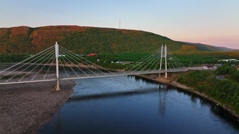 Drone-flying-in-front-of-the-Sami-Bridge-and-Teno-river,-summer-sunset-in-Utsjoki