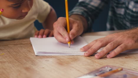 Nahaufnahme-Des-Vaters-Zu-Hause-In-Der-Küche-Am-Tisch,-Der-Seinem-Sohn-Bei-Den-Hausaufgaben-Hilft