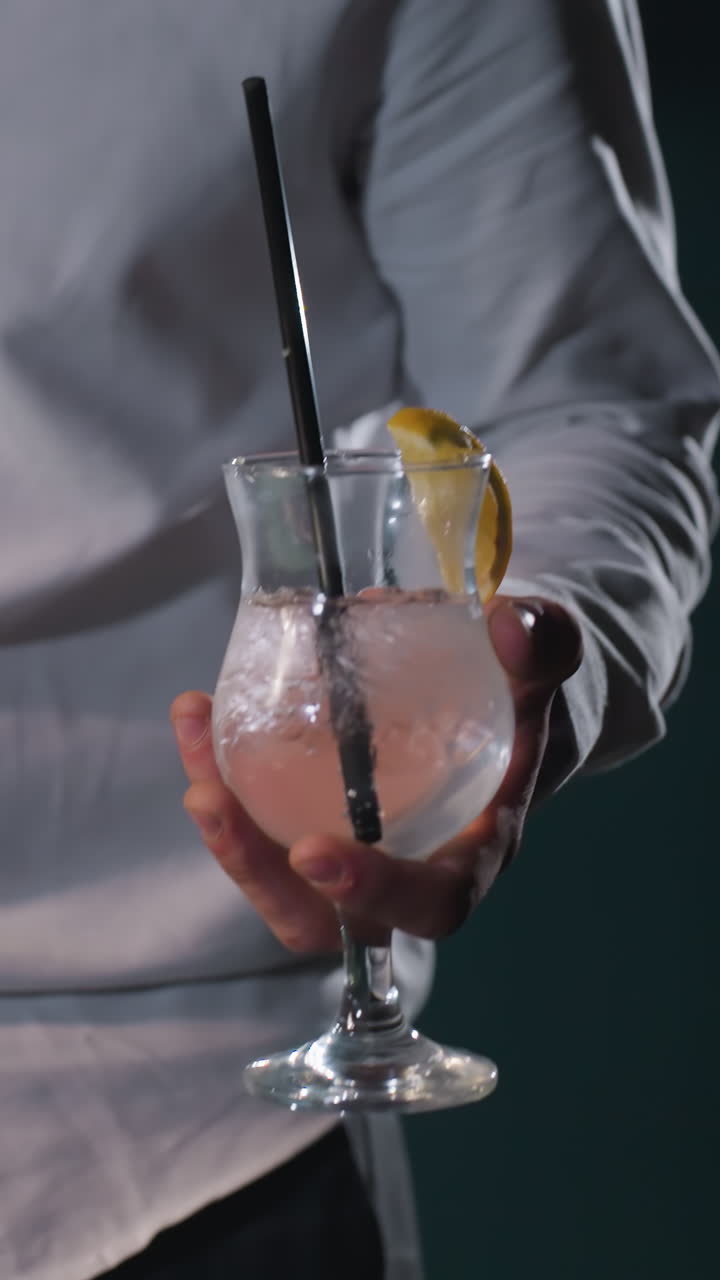 Persona con camicia bianca e pantaloni grigi, volto non visibile, che tiene in mano una stecca da biliardo e un bicchiere di limonata con cannuccia nera. Cubetti di ghiaccio e una fetta di limone galleggiano nel bicchiere, creando un aspetto rinfrescante.