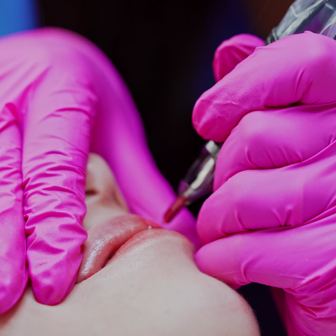 Lips micropigmentation. Cosmetologist applying permanent makeup on lips with a tattoo machine. Cosmetology procedure. Close-up.