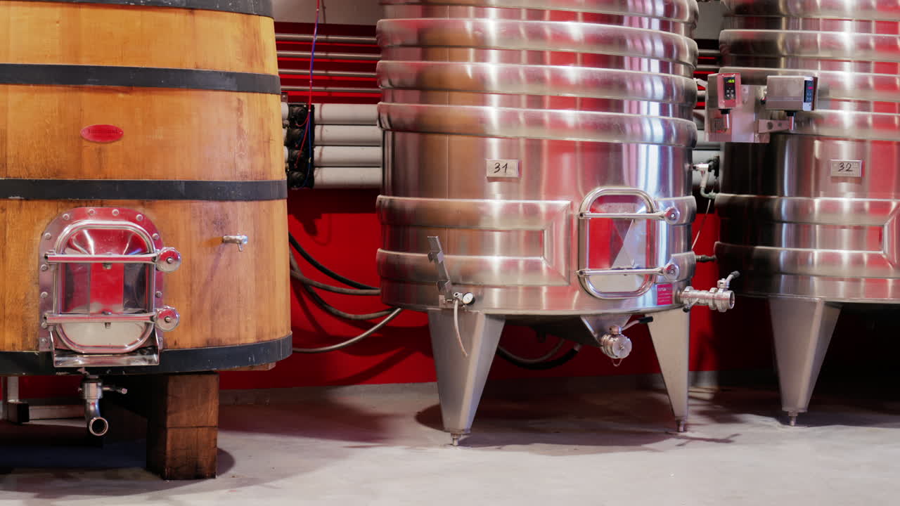 Nice, France - May 17, 2025: Wooden wine barrel near a stainless steel tanks at the Chateau de Cremat winery