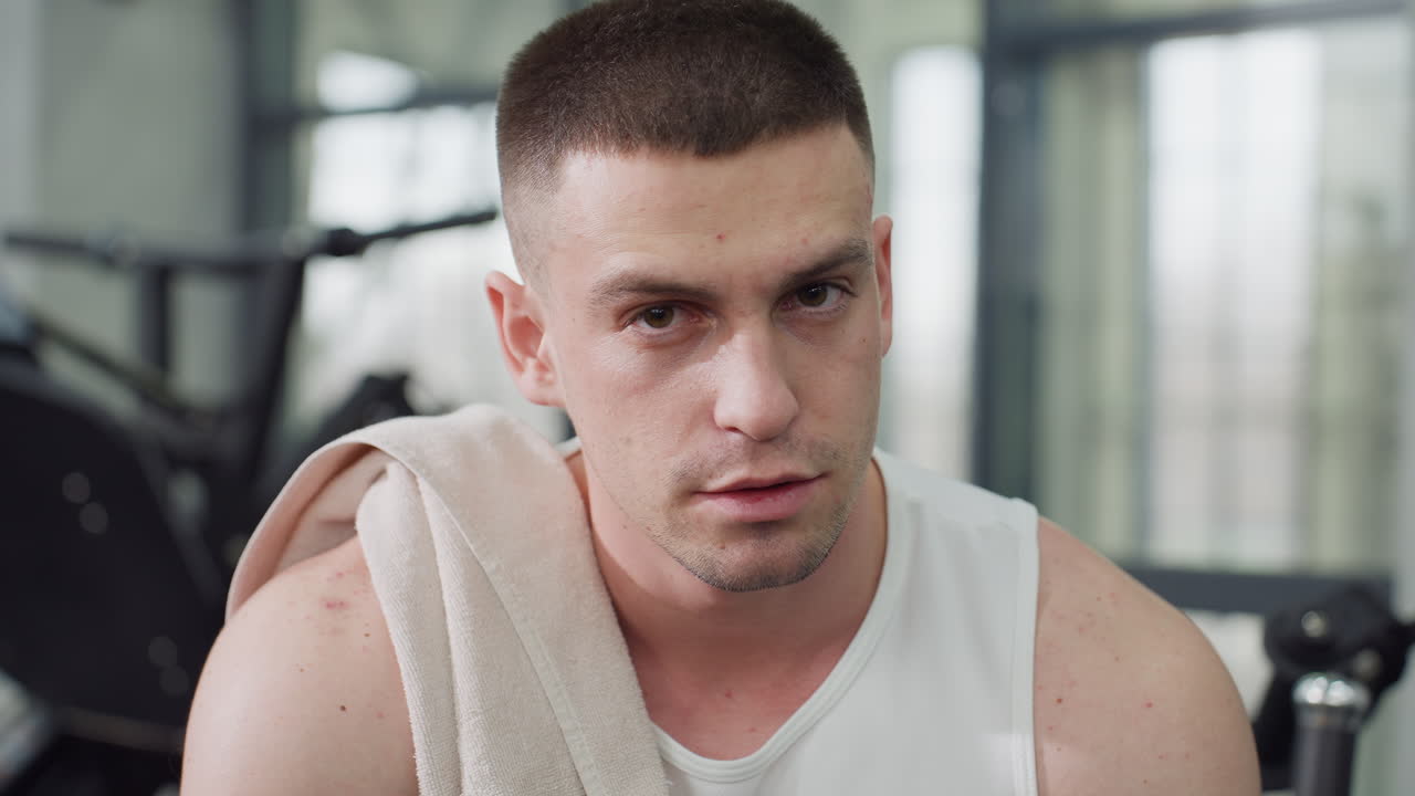 Portrait view of fitness fanatic resting on weight bench after intense chest press session exhaling in relief with towel draped over shoulder under gym lighting showing post workout recovery moment