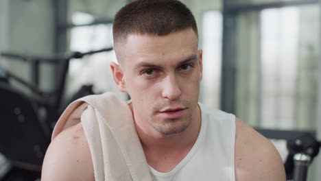portrait view of fitness fanatic resting on weight bench after intense chest press session exhaling in relief with towel draped over shoulder under gym lighting showing post workout recovery moment