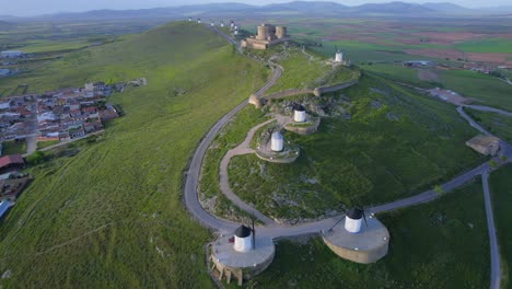 Scenic-top-aerial-view-of-old-windmills-and-castle-on-top-of-hill-at-sunrise,-Spanish-historical-tourism