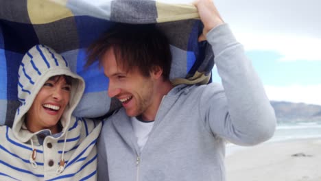 Happy-couple-hiding-in-blanket-at-beach