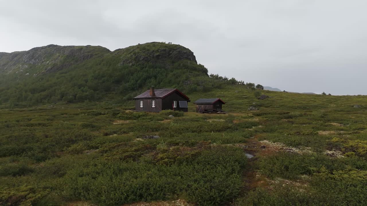 Aerial view of a wood cabin nestled on a grassy mountain hill, surrounded by serene natural beauty and tranquility. orbit motion shot