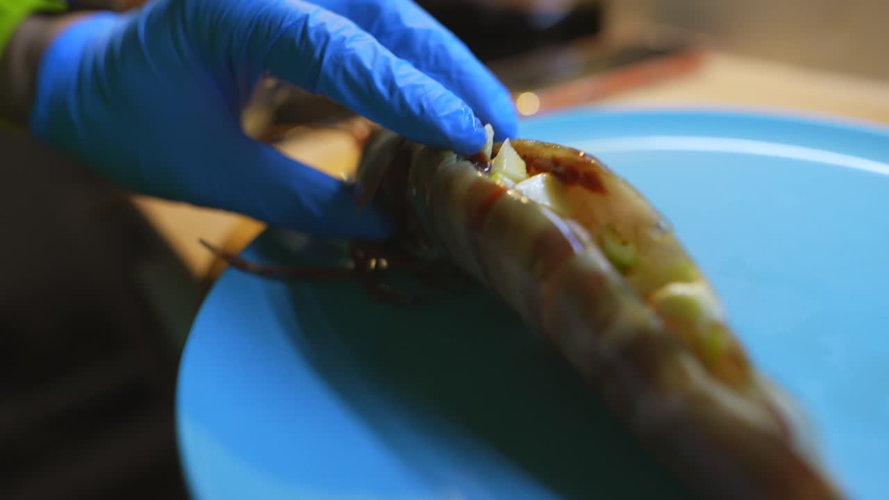 Chef's Gloved Hand Preparing Raw Shrimp on a Blue Plate