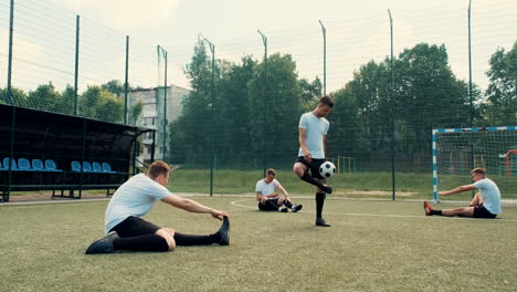 young street football player training freestyle tricks while his team sitting on the pitch doing stretch exercises