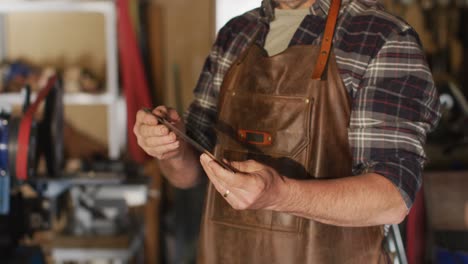 midsection of caucasian male knife maker in workshop, holding knife