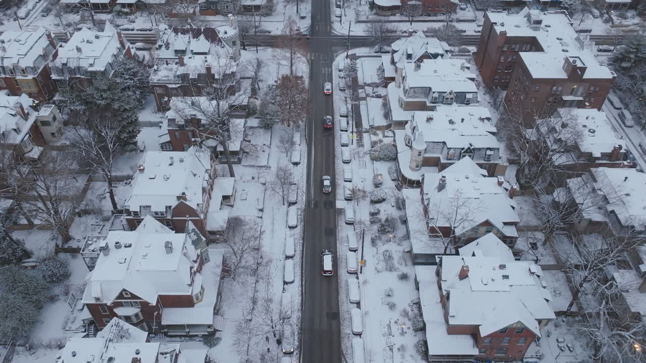Aerial footage following a line of cars driving down a street through snow covered neighborhoods in West Philadelphia, Pennsylvania.