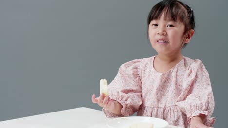 Asiatic-child-eating-piece-of-sweet-in-studio-with-gray-background