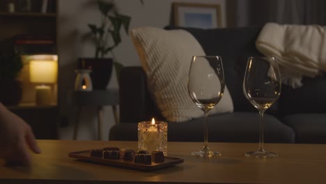 hombre planeando una velada romántica en casa en el salón con vino y chocolates