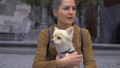 slow-motion footage of a young woman holding a spitz dog, with a fountain in the background