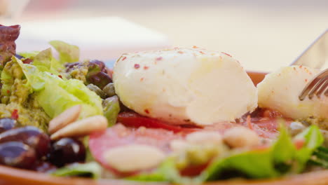 a close-up shot of a salad featuring mozzarella, fresh tomatoes, and lettuce, with cutlery cutting into the mozzarella, presenting a delightful dining experience