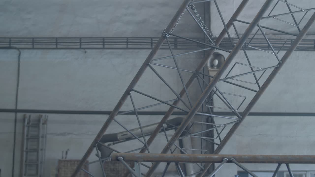 Large metal structure secured with chains is slowly lifted. Sparks and welding smoke underneath.