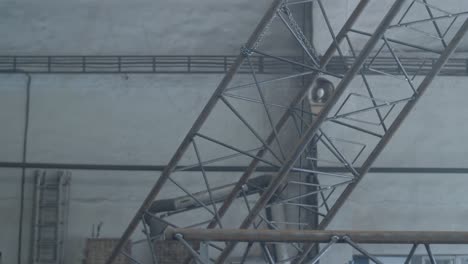large metal structure secured with chains is slowly lifted. sparks and welding smoke underneath.