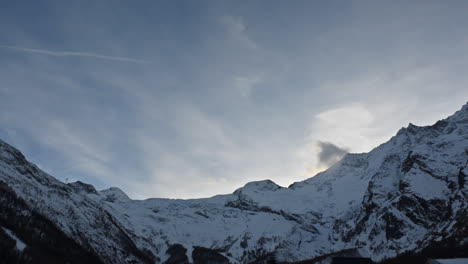 Timelapse:-Gran-Vista-De-Una-Cadena-Montañosa-En-Los-Alpes-Suizos,-Saas-Fee,-Cumbres-Rocosas-Nevadas-Por-La-Noche,-Nubes-En-Movimiento