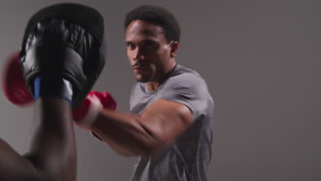 Studio-Shot-Of-Male-Boxer-Sparring-Working-Out-With-Trainer-Wearing-Punch-Mitts-Or-Gloves-Practising-For-Fight-9