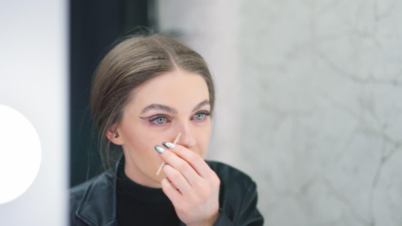 Woman applying or adjusting her eyeliner while looking in a mirror