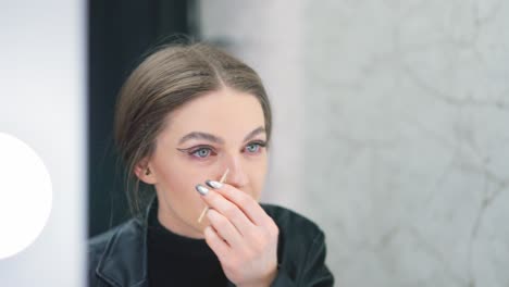woman applying or adjusting her eyeliner while looking in a mirror