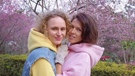 two women hugging in a cherry blossom park