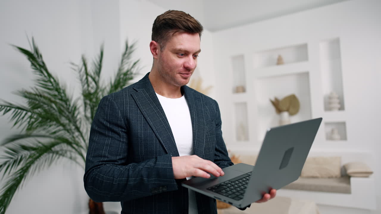 Modern positive business person using technology in work. Man in jacket uses laptop standing indoors.