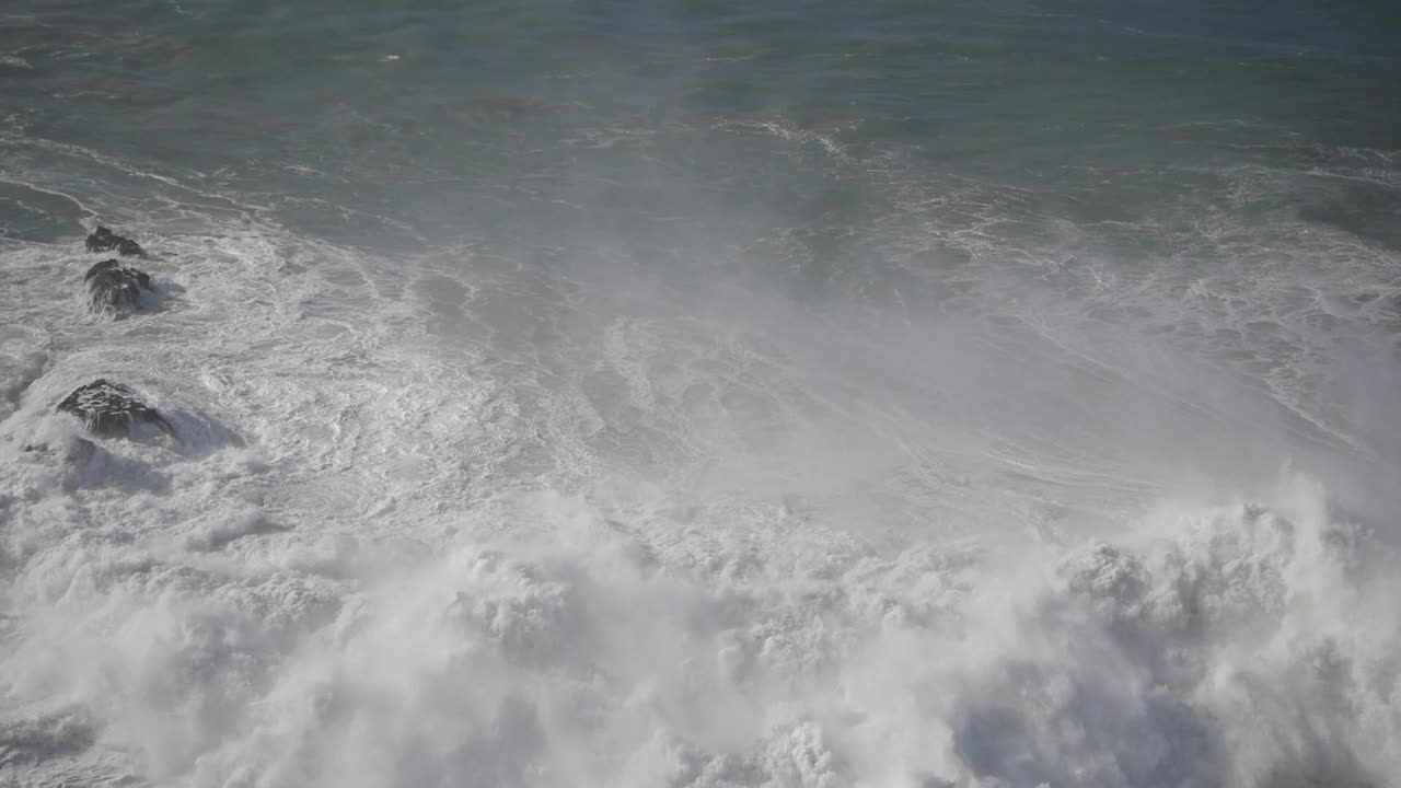 A powerful wave crashes over dark rocks at Praia do Norte in Nazare, Portugal