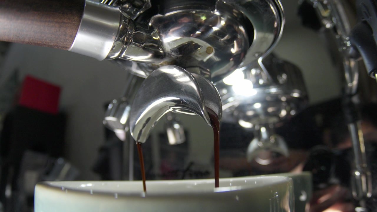Close-up em ângulo de um porta-filtro de máquina de café expresso extraindo café fresco e escuro em uma xícara. Perfeito para branding de café, hotelaria e conteúdo de estilo de vida matinal