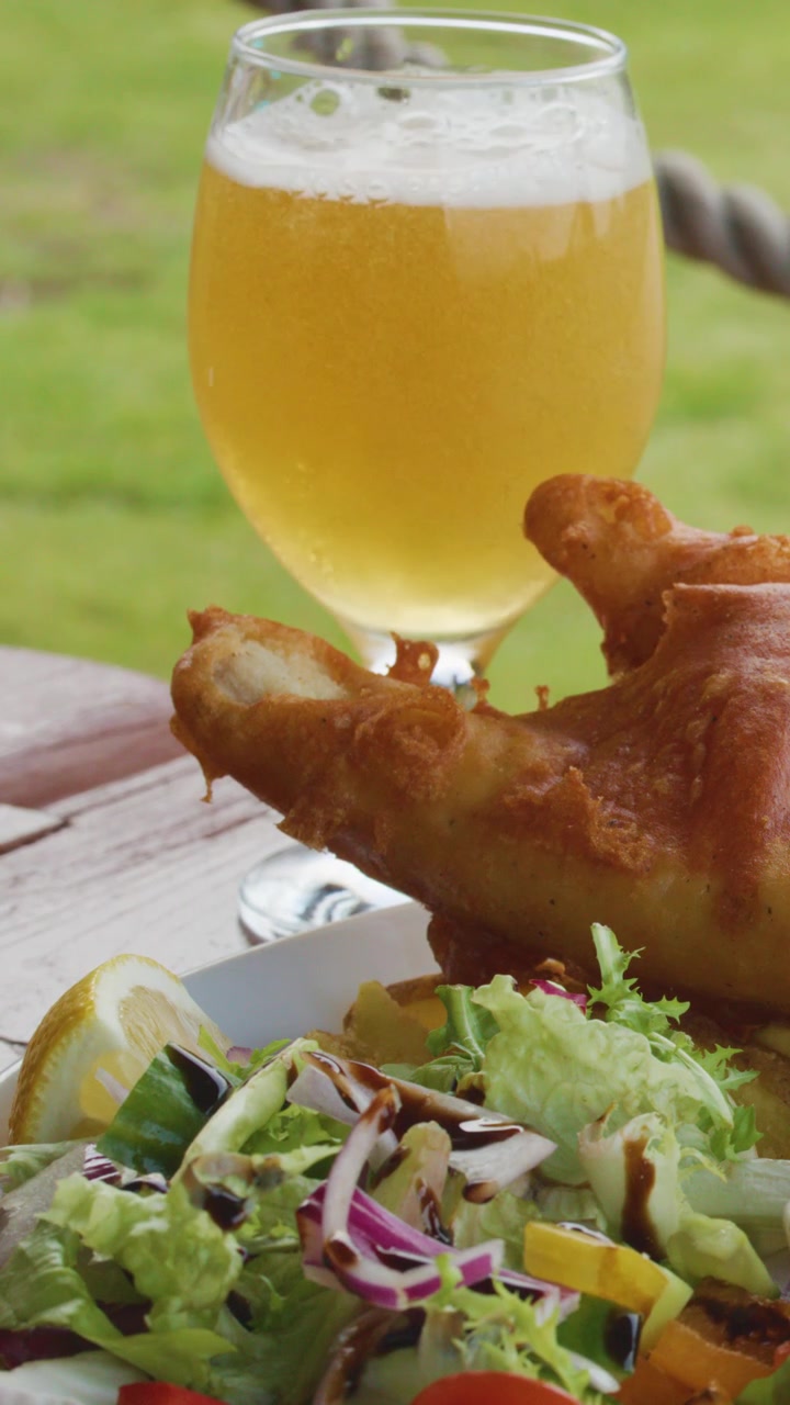 Sirviendo cerveza dorada en un vaso junto a pescado frito y ensalada