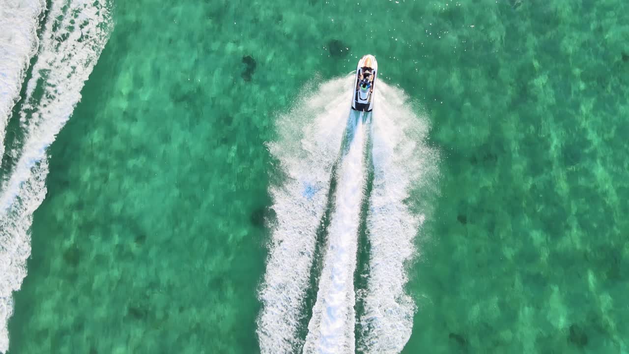 Aerial bird's eye view of a couple riding a jet ski over crystal clear ocean water