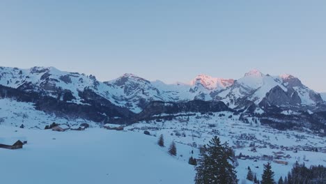 Mit-Einer-Drohne-Aufgenommenes-Filmmaterial-Zeigt-Die-Bezaubernde-Schönheit-Des-Sonnenaufgangs,-Der-Einen-Goldenen-Farbton-Auf-Die-Silhouette-Einer-Schneebedeckten-Bergkette-Wirft