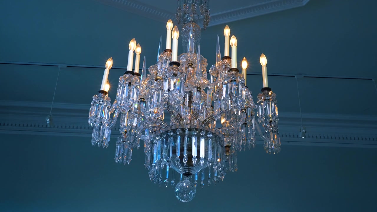Lampadario di cristallo ornato con luci a forma di candela luminose. Vista dal basso di un lampadario di cristallo decorativo illuminato con lampadine elettriche a forma di candela contro un soffitto blu